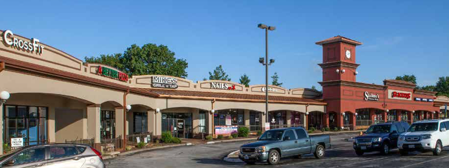 A strip mall with various stores and cars parked in front
